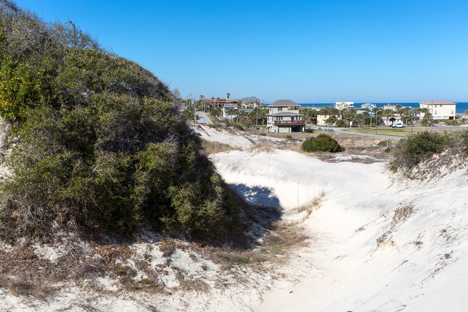 a large dune over looks beach house and the ocean