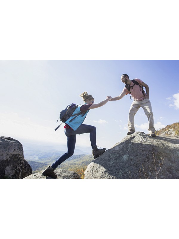 A man extends his hand on top of a rock to a woman below.