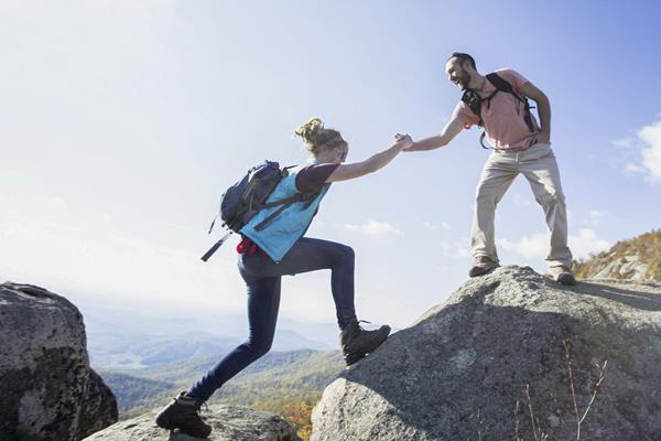 A man extends his hand on top of a rock to a woman below.