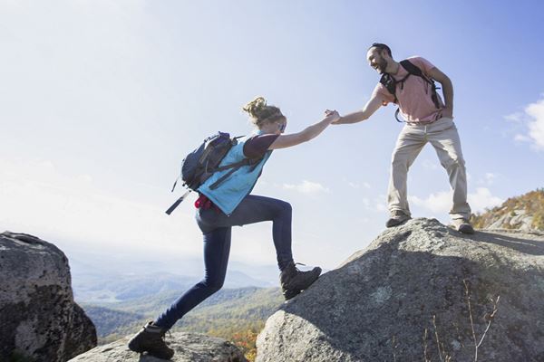 A hiker on top of a boulder reaches down to help another up, in the rock scramble on Old Rag.