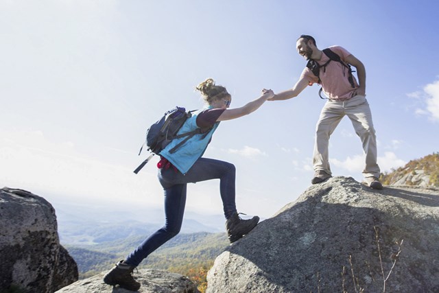 A man extends his hand on top of a rock to a woman below.