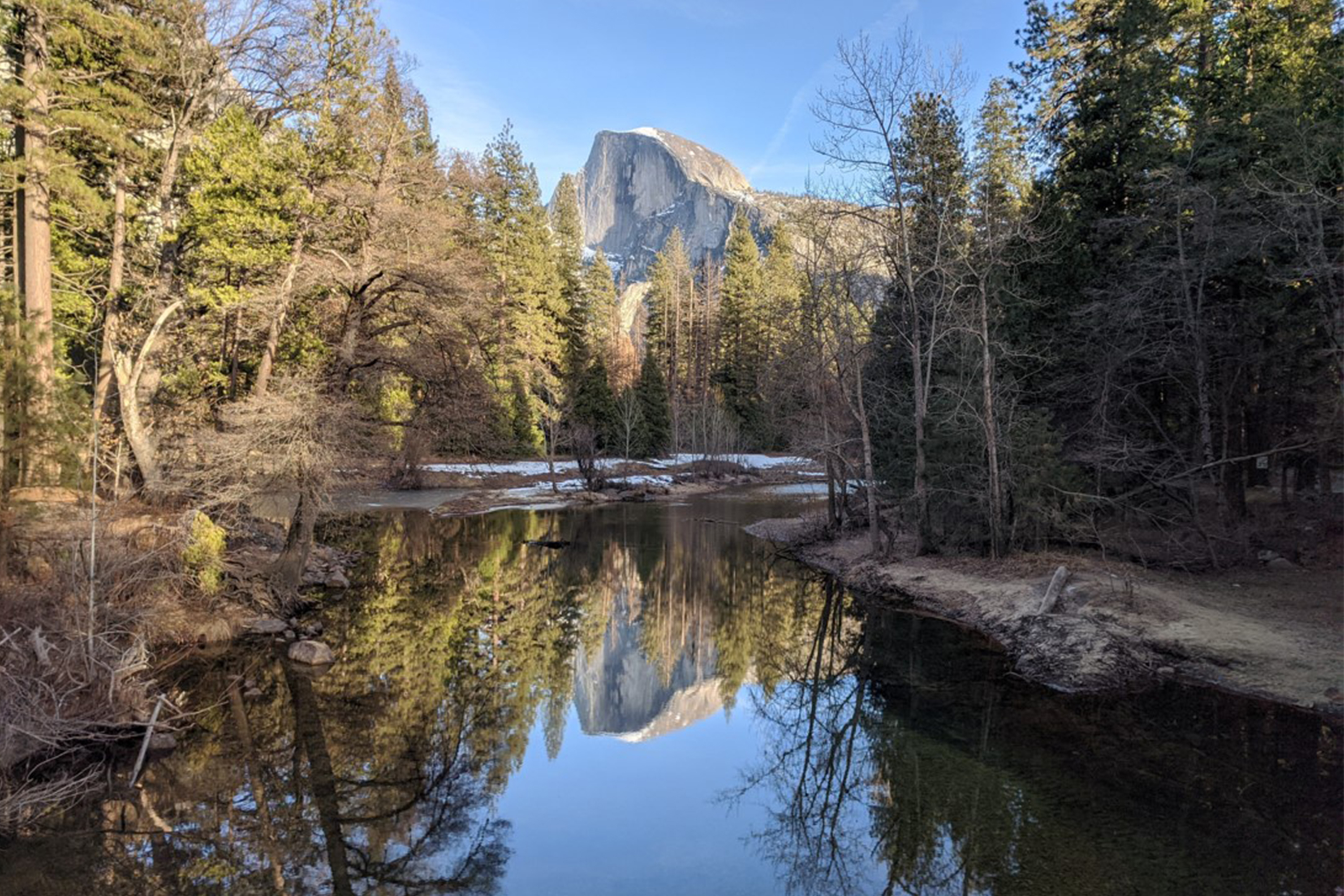 A large granite formation reflects in still water surrounded by trees