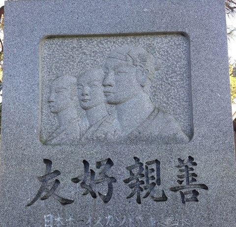 A photo of a stone monument with a carving of three Japanese sailors and text in Japanese.