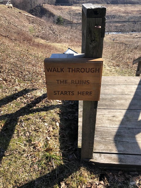 A wooden sign that says a Walk Through the Ruins starts here.