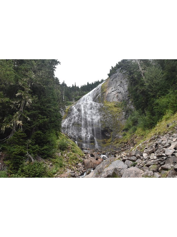 Veil-like waterfall cascades over large cliff with small boulders in foreground