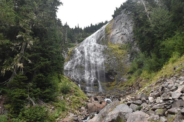 Veil-like waterfall cascades over large cliff with small boulders in foreground