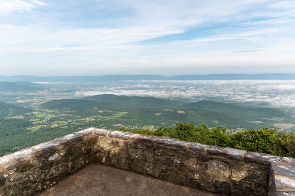 A stone platform with a view of a valley below and blue mountains beyond.