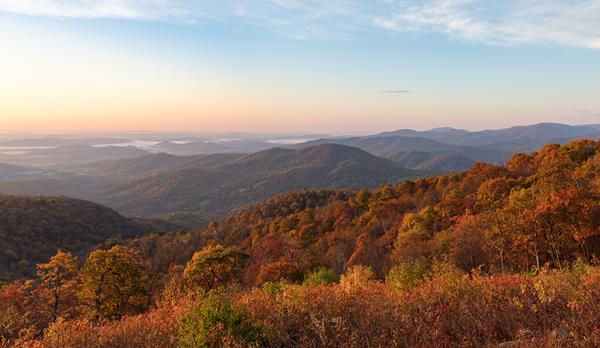 A view from an overlook down into a valley below filled with fall colors of red and orange.