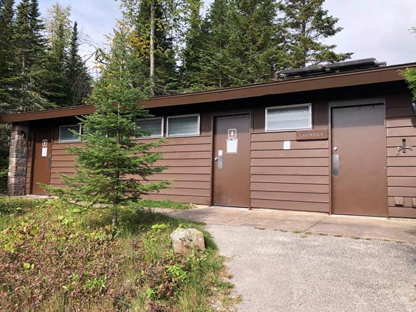A paved path leads to a bathroom building surrounded by trees.