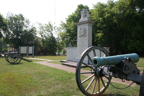 White granite monument with a carved eagle on top with 2 civil war cannons flanking monument
