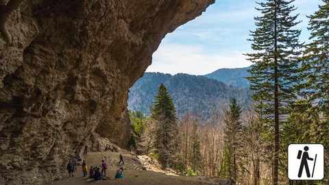 A cave like overhang over a trail with a mountain view.