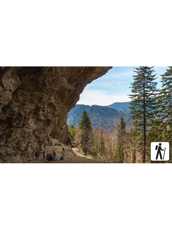 A cave like overhang over a trail with a mountain view.