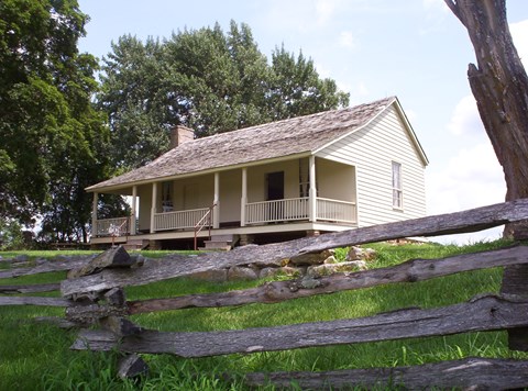 Ray House in the summer with split rail fencing at the border of yard in front of wire road path