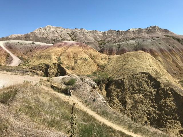 A small trail winding through rolling mounds striped yellow, red, white and brown