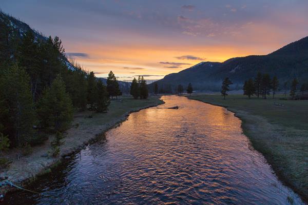 Purple, pink, and orange are cast across the sky and reflect in the slowly moving water of a river.