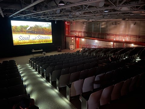 Movie title displaying "Steel and Steam" on screen and dimly lit theater