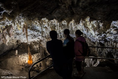 Three people looking over a railing at glowing cave formations