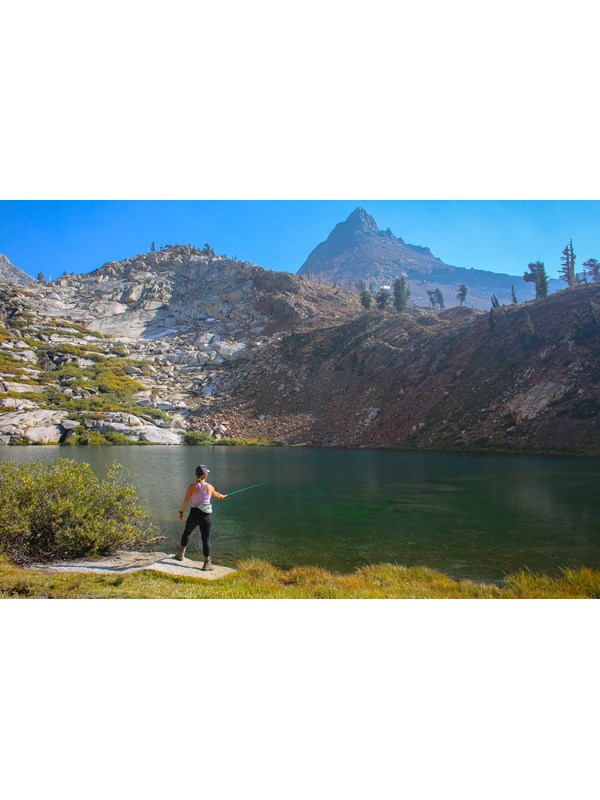 A woman fishing in an alpine lake surrounded by granite walls.