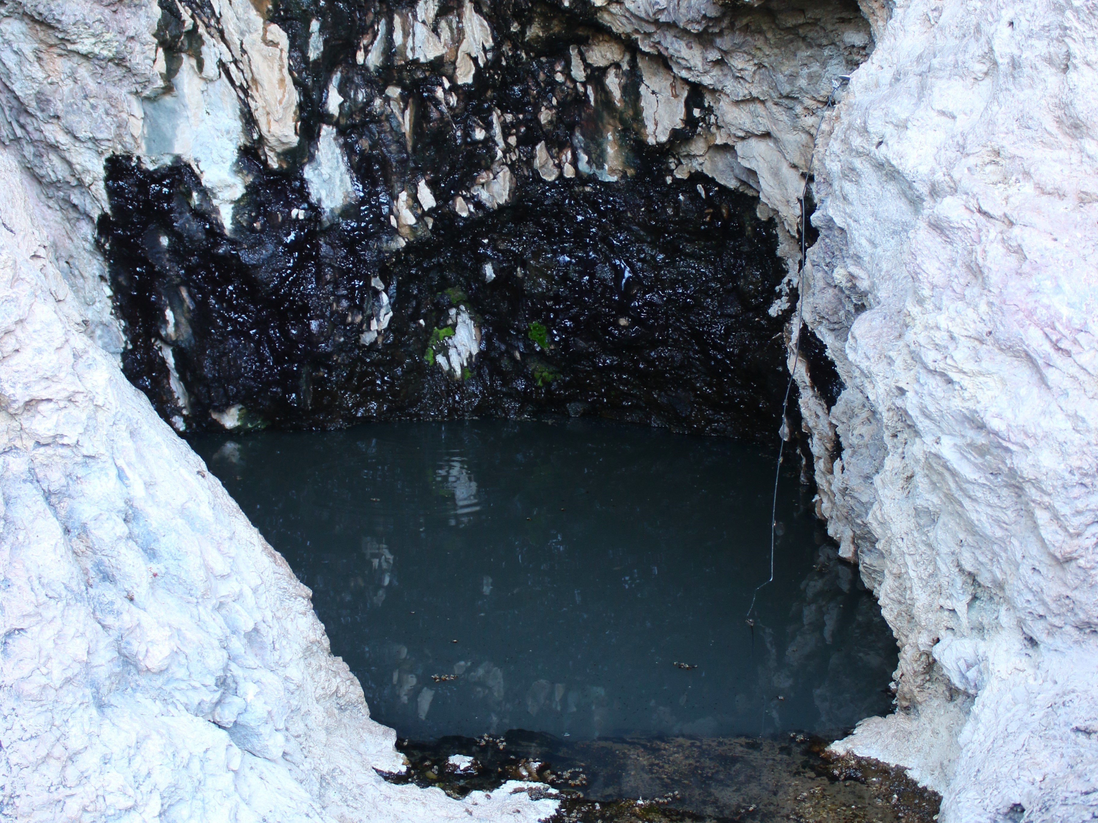 A deep pool of water is nestled in white rocks. The wall behind the water is black from moisture.