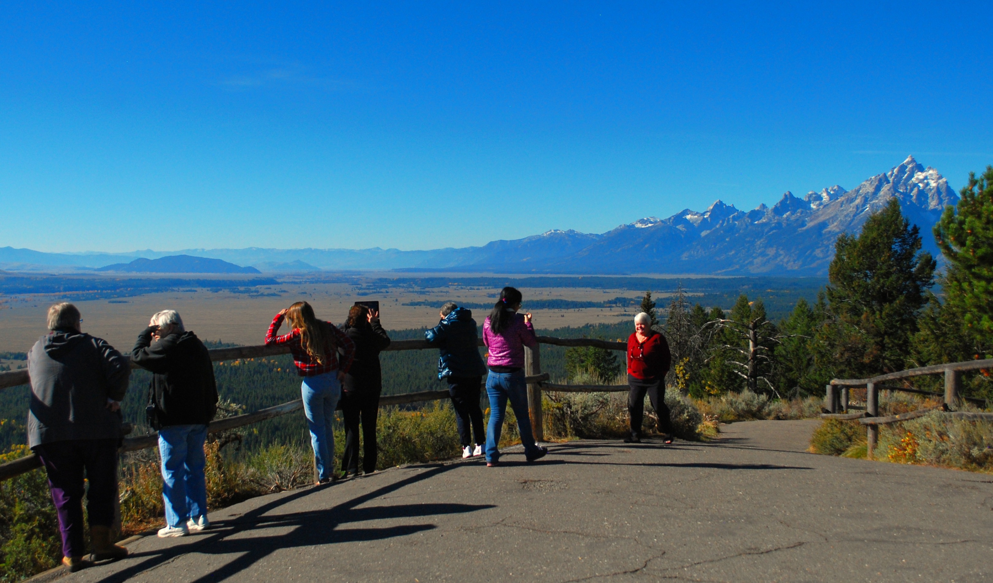 A group of seven people enjoy the views and take pictures of the valley and mountains.