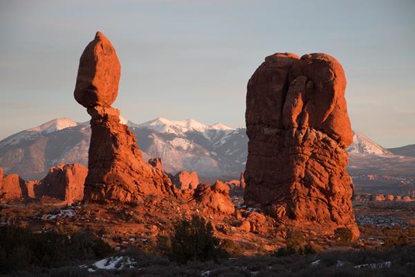 Sandstone boulder atop a its pedestal glows bright orange at sunset, snowy peaks in background
