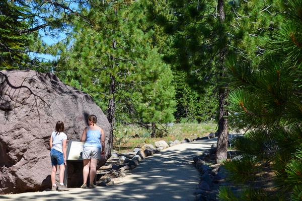 A girl and a woman stand next to a boulder and interpretive sign on a walkway.