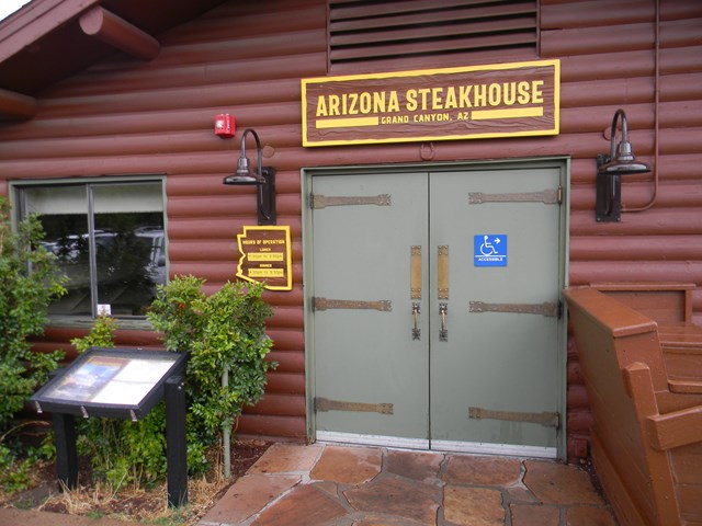 A large sign above a pair of metal double doors set in a wooden log wall reads "Arizona Steakhouse".