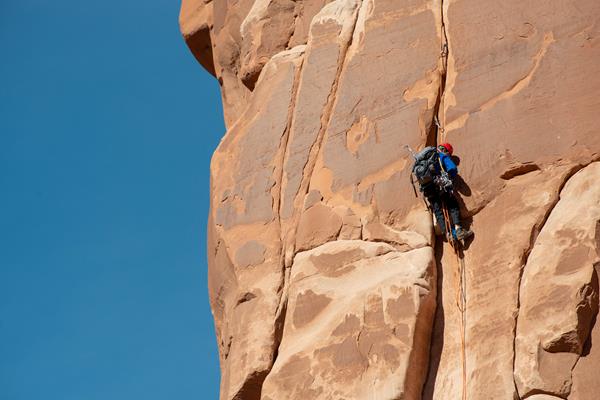 rock climber on vertical tan sandstone face, blue sky in background