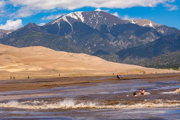 Children playing in a wave surging down a wide creek at the base of the dunes and mountains