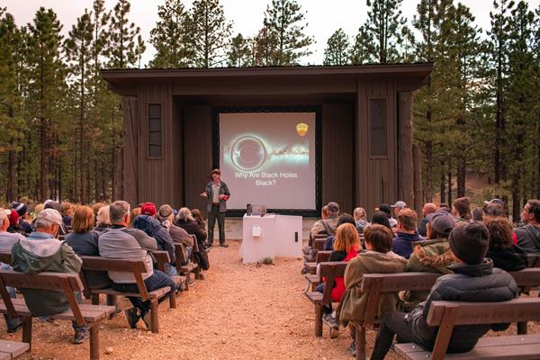 A ranger stands in front of a screen before a seated audience.