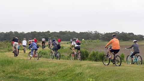 A large group of bike riders on an elevated grassy trail.