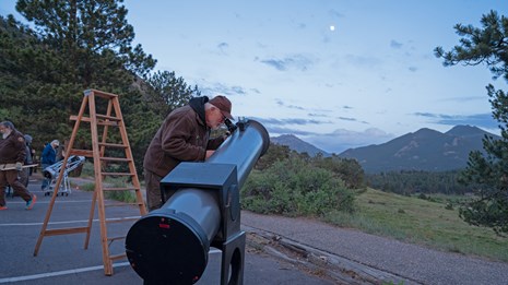 An NPS night sky volunteer is looking at the stars with a telescope