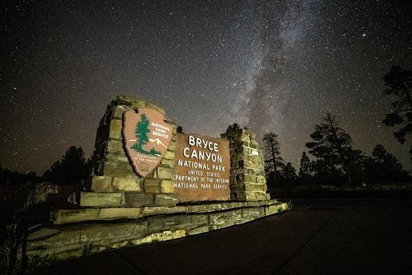 An illuminated Bryce Canyon park entrance sign against a backdrop of stars in a dark sky