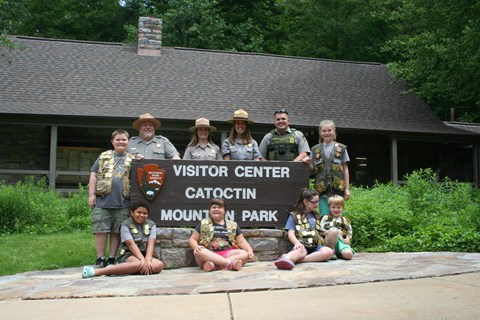 A group of park rangers and children posing around a visitor center sign.