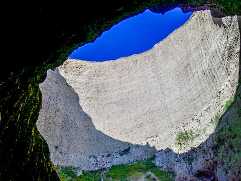 Looking up at blue sky visible through a large circular hole in the roof of a sea cave.