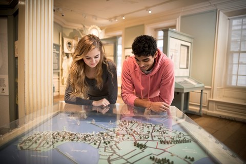 Two youth in an exhibit space, leaning over an interactive map table and looking down at it.