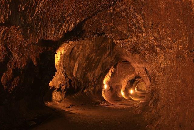 A lava tube lit by orange electric light, surrounded by rainforest