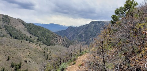 A trail leading around a cliff edge with a view of mountains