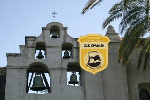 A junior ranger badge on an picture of a historic Spanish mission