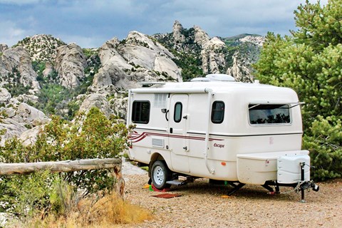 A small bumper pull camper parked with a spectacular view of distant granite formations.