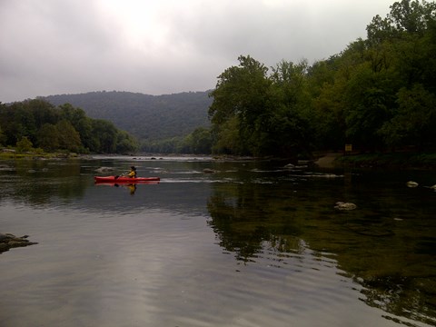 kayaker on a calm, wide river with forested hillsides on both shorelines
