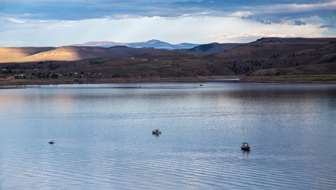 Multiple boats on a still water reservoir with mountains in the background