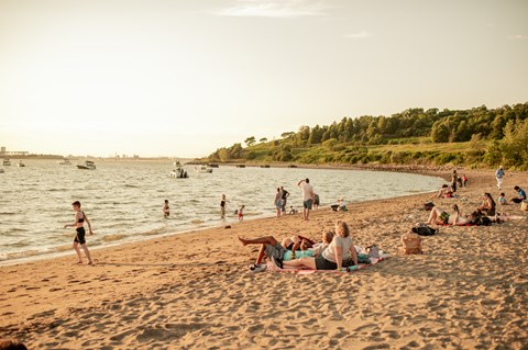 view of the Spectacle beach at sunset with people on the beach and swimming in the water.