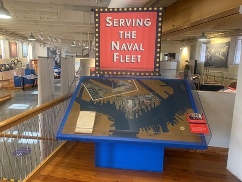 Exhibit display of map of Charlestown Navy Yard with "Serving the Navel Fleet" sign hanging behind.