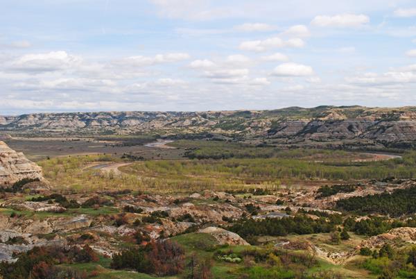 A river meanders through cottonwood trees and steep buttes.
