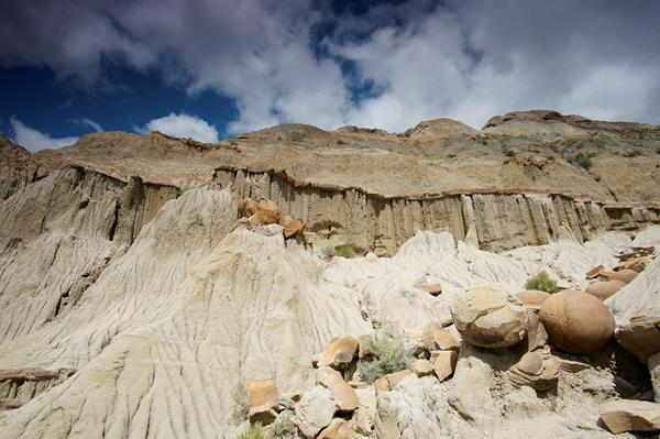 Several large round rocks eroded out of the side of a butte. The sky above the butte is cloudy blue.