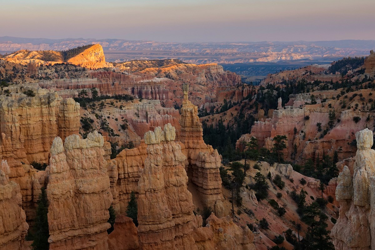 A vivid landscape of red, pink, orange, and white rock spires stands before a hazy horizon