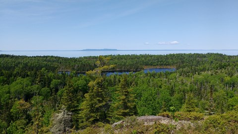 View from a ridge overlooking an interior lake, a forest, Lake Superior, and Canada's shoreline.