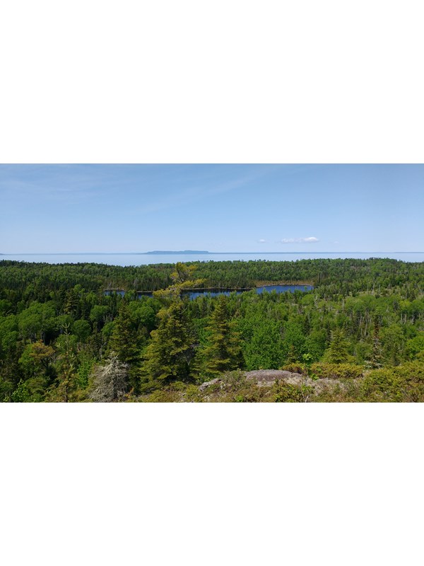 View from a ridge overlooking an interior lake, a forest, Lake Superior, and Canada's shoreline.