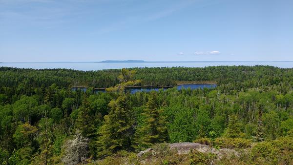 View from a ridge overlooking an interior lake, a forest, Lake Superior, and Canada's shoreline.